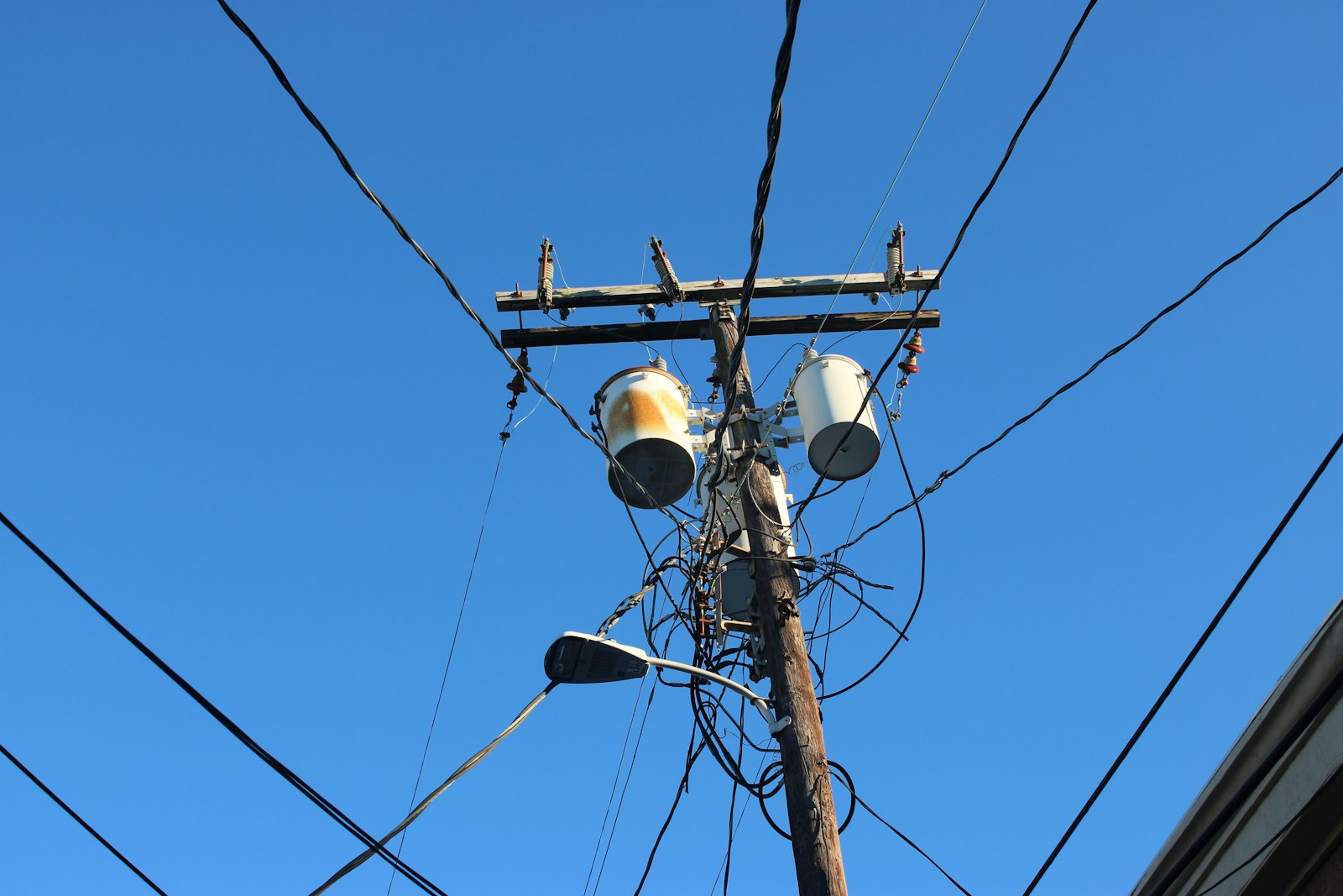 Utility transformers and a web of overhead power lines against a clear sky.